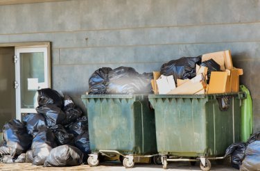 Grüne Abfallcontainer im Außenbereich, die mit Müll überfüllt sind
